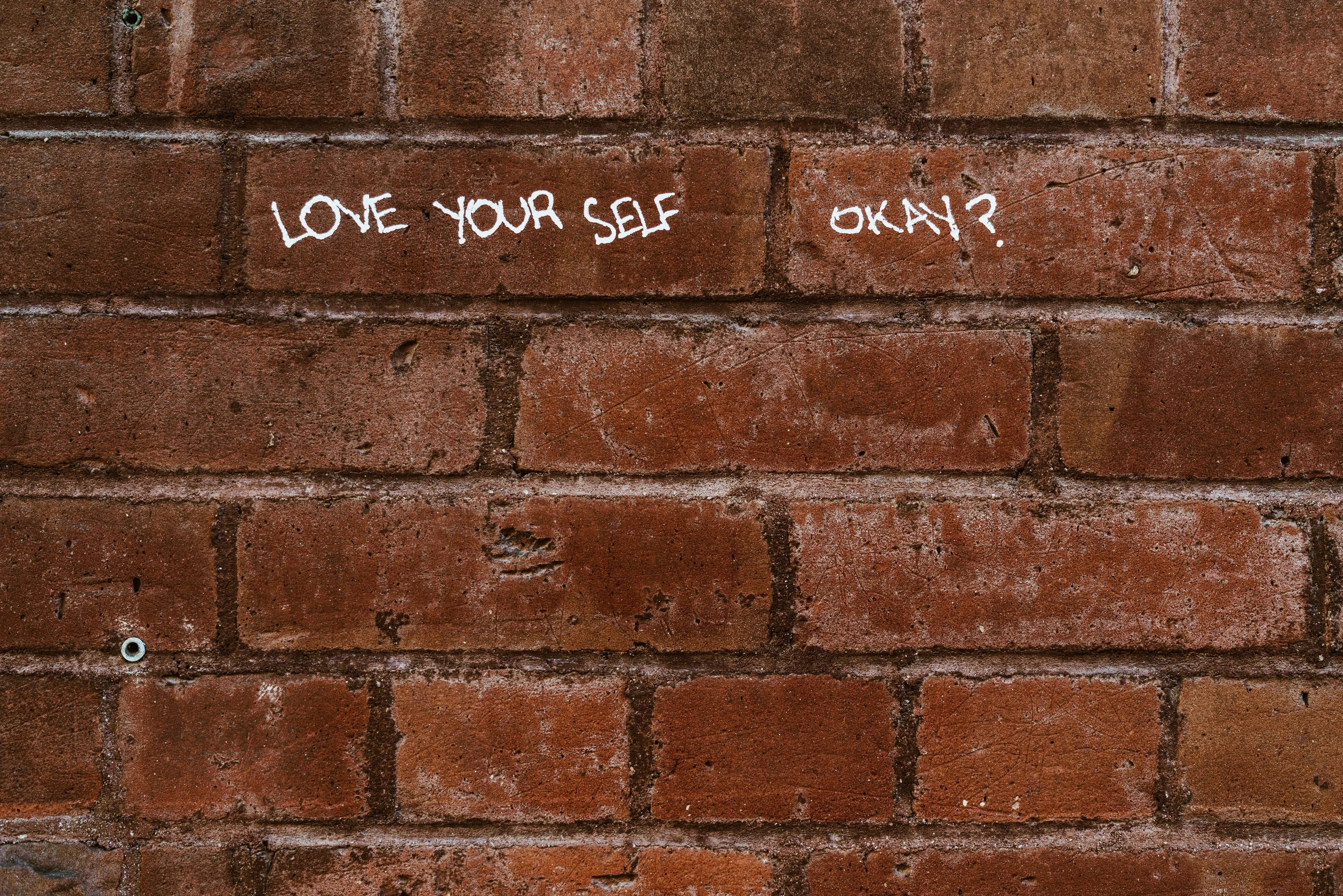 A brick wall with 'love yourself okay?' drawn on it